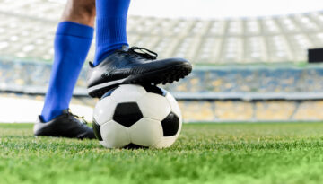 legs of professional soccer player in blue socks and soccer shoes on ball at stadium